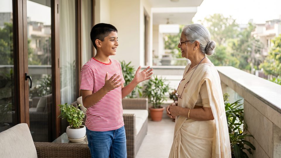 A boy explains a science idea to his smiling grandmother on a sunny balcony