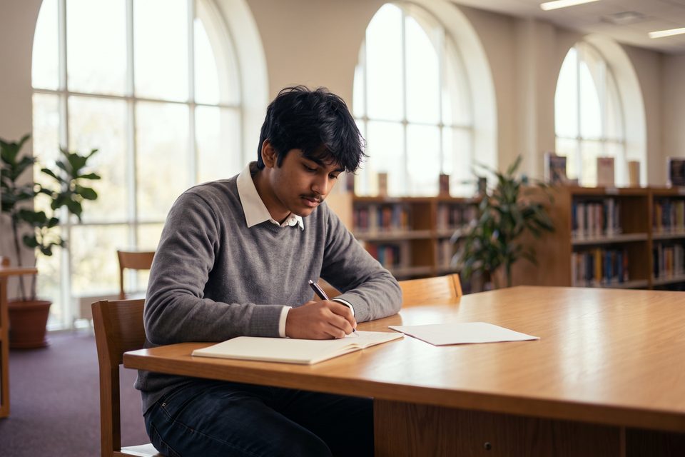 A teenage boy works through a reasoning problem at a library table
