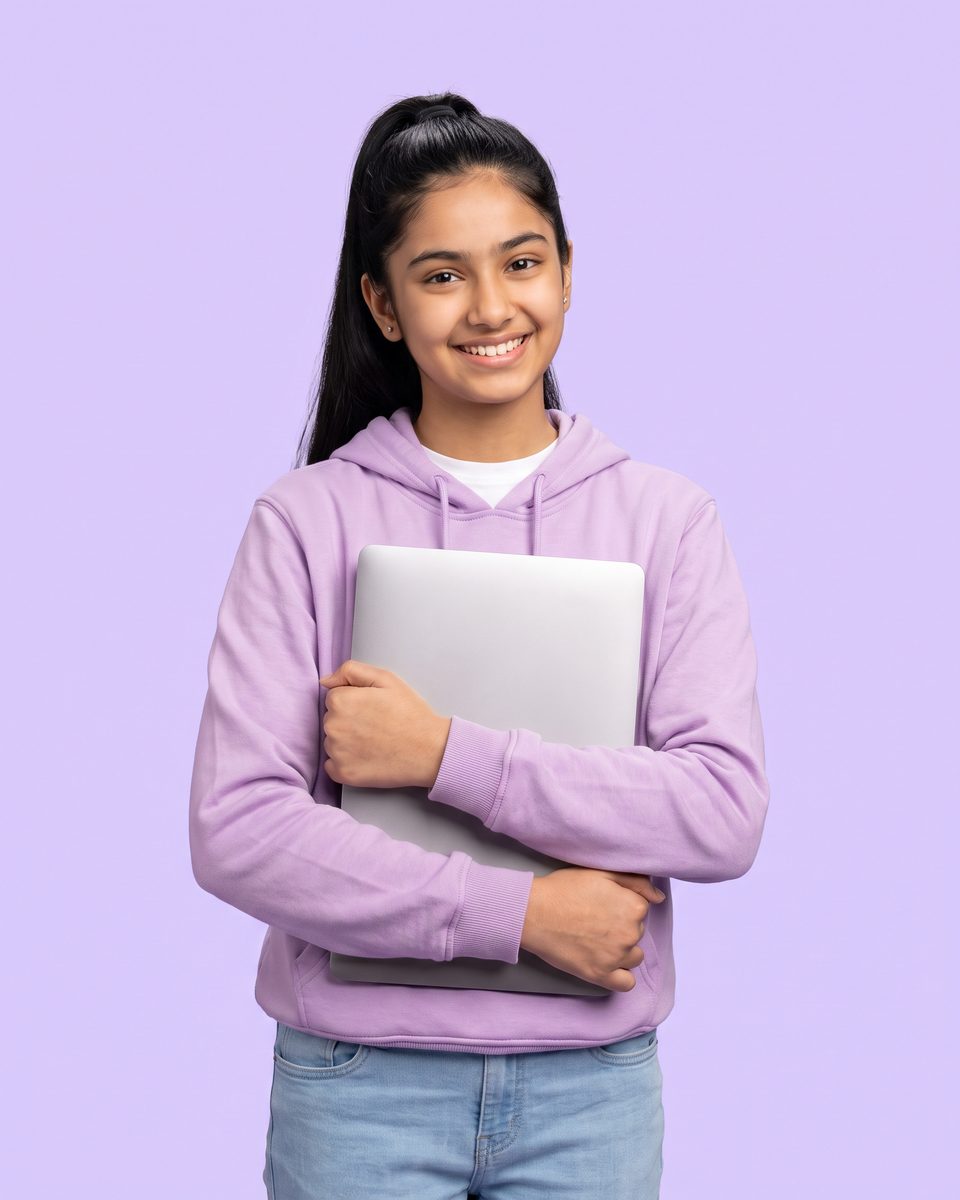 A 14-year-old girl in a lilac hoodie smiles, holding a laptop
