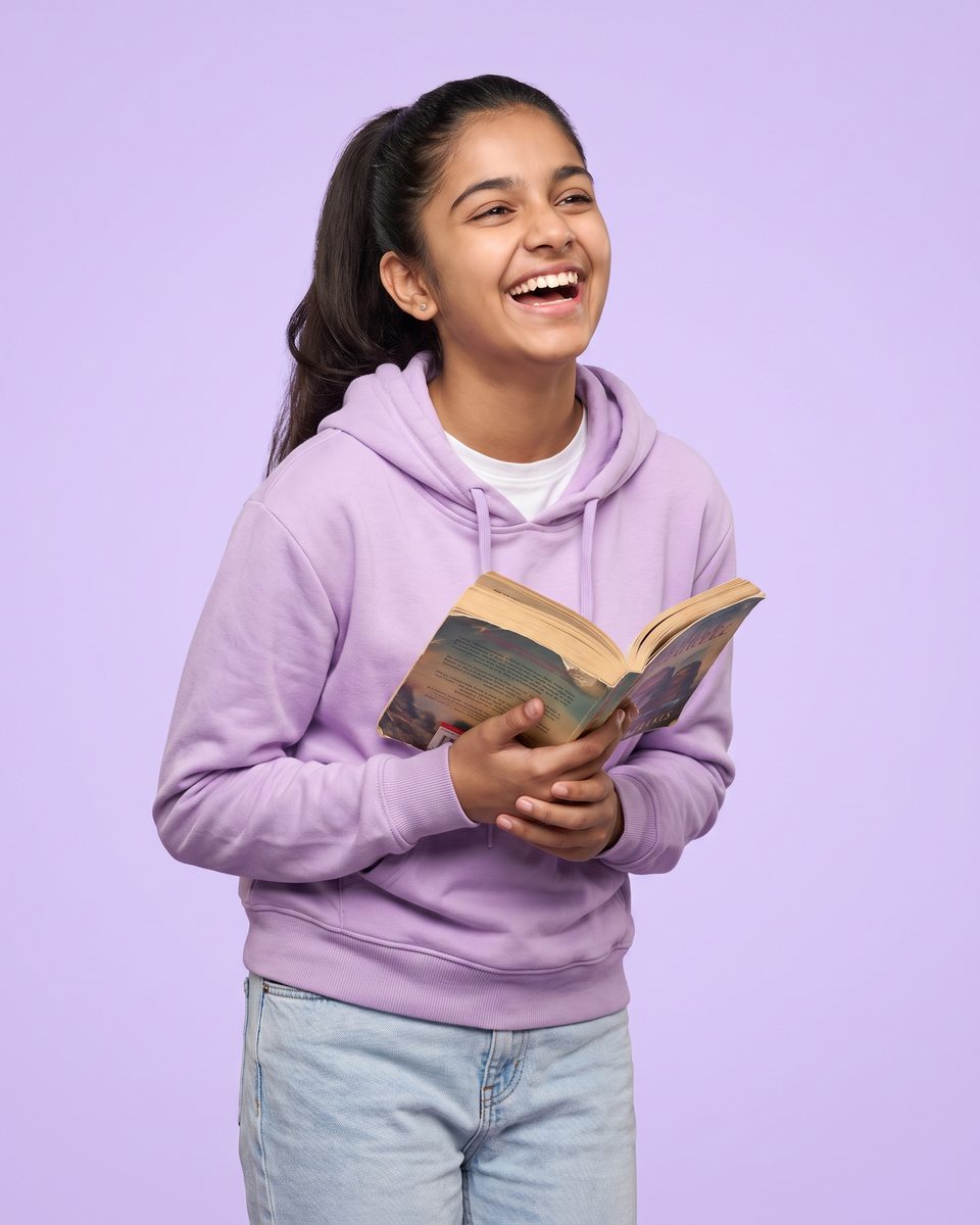 A laughing 14-year-old girl holds an open novel to her chest