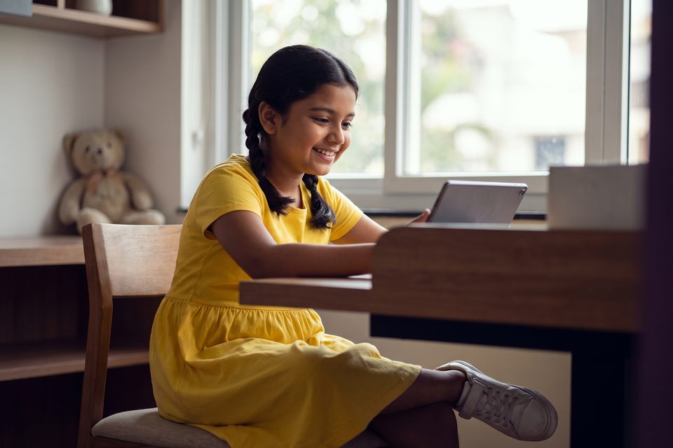 A young girl learns happily on a tablet in a calm, bright study corner