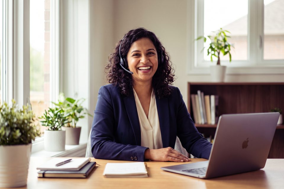 A smiling tutor with a headset teaches online from a bright home desk
